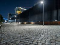 a brick paved street next to a building and a construction crane above it at night