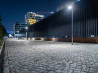 a brick paved street next to a building and a construction crane above it at night