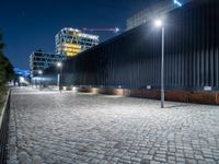 a brick paved street next to a building and a construction crane above it at night