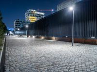 a brick paved street next to a building and a construction crane above it at night