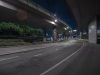 an empty street in front of a bridge lit up at night with the lights on