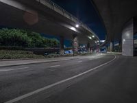 an empty street in front of a bridge lit up at night with the lights on