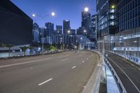 a long empty street lined with traffic lights and tall buildings next to the roadway and a road at dusk