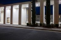 an empty office building at night with rows of trees and plants outside the doors and windows