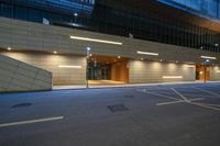 an empty city street in front of the office building with lights on at night time