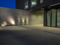 large cement wall with lights in front of a building at dusk with patio area lit up