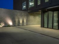 large cement wall with lights in front of a building at dusk with patio area lit up