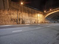 two streets with arches lit up at night by street lights and wall with graffiti under