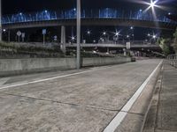 an empty street and parking area at night, illuminated by street lights and overpasses