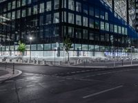 an empty street at night in front of a very modern building in the city with windows