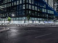 an empty street at night in front of a very modern building in the city with windows