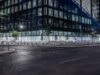 an empty street at night in front of a very modern building in the city with windows