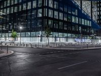 an empty street at night in front of a very modern building in the city with windows