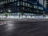 an empty street at night in front of a very modern building in the city with windows