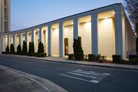 a large building next to the street with a tree lined walkway behind it at dusk