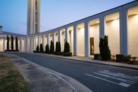 a large building next to the street with a tree lined walkway behind it at dusk