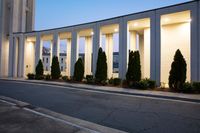 a large building next to the street with a tree lined walkway behind it at dusk