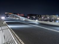 a bridge over water with buildings in the background at night time and no traffic, or people