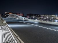 a bridge over water with buildings in the background at night time and no traffic, or people