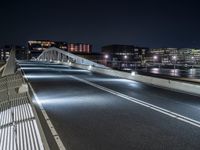 a bridge over water with buildings in the background at night time and no traffic, or people