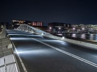 a bridge over water with buildings in the background at night time and no traffic, or people