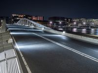 a bridge over water with buildings in the background at night time and no traffic, or people