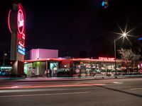 a neon sign for the drive thru restaurant at night time with blurred cars in the foreground