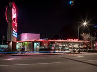 a neon sign for the drive thru restaurant at night time with blurred cars in the foreground