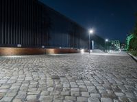 a brick road in the night with lights on, and a building beside it on a street corner