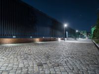 a brick road in the night with lights on, and a building beside it on a street corner