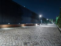 a brick road in the night with lights on, and a building beside it on a street corner