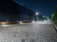 a brick road in the night with lights on, and a building beside it on a street corner