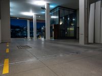 the parking meter is on a road as it passes by a large office building and is lit up at night