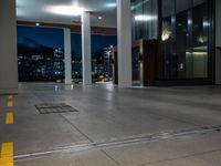 the parking meter is on a road as it passes by a large office building and is lit up at night