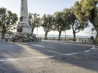 a city park with trees and large rocks and a monument on the corner, while parked cars are waiting near the curb