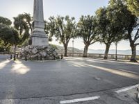 a city park with trees and large rocks and a monument on the corner, while parked cars are waiting near the curb