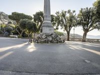 a city park with trees and large rocks and a monument on the corner, while parked cars are waiting near the curb