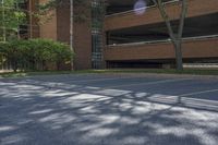 an empty parking lot outside an apartment building, with cars parked in it, outside, with bright sun and tree shadows