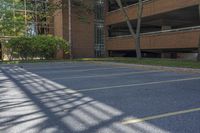 an empty parking lot outside an apartment building, with cars parked in it, outside, with bright sun and tree shadows