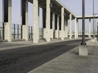 a parking lot with columns and a walkway between two building fronts that span the sky