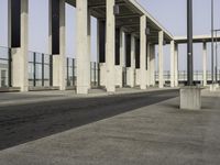 a parking lot with columns and a walkway between two building fronts that span the sky