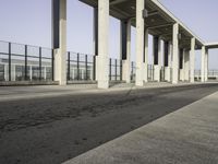 a parking lot with columns and a walkway between two building fronts that span the sky