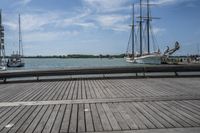 the pier in the harbor with two sailboats and benches for seating on the water
