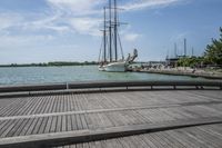 the pier in the harbor with two sailboats and benches for seating on the water