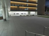 a concrete plaza at night with a metal railing and a building in the background at night