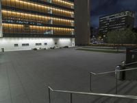 a concrete plaza at night with a metal railing and a building in the background at night
