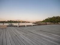 a boardwalk with benches and water in the foreground at dusk of a city by a river