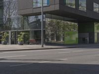 this is a bus stop on the street that is next to the building and some trees