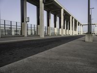 street by a concrete structure with pillars and lamps on it, leading to the train station