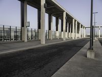 street by a concrete structure with pillars and lamps on it, leading to the train station